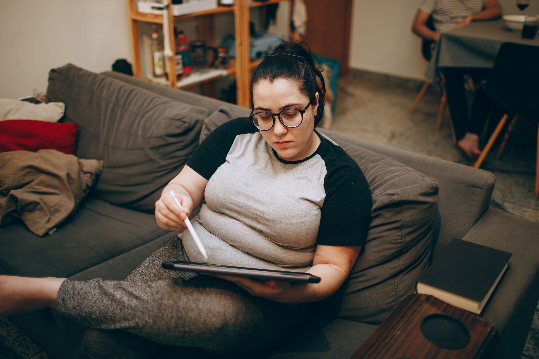 Femme se relaxant sur un canapé, utilisant un stylet numérique sur une tablette, idéal pour le travail à distance.